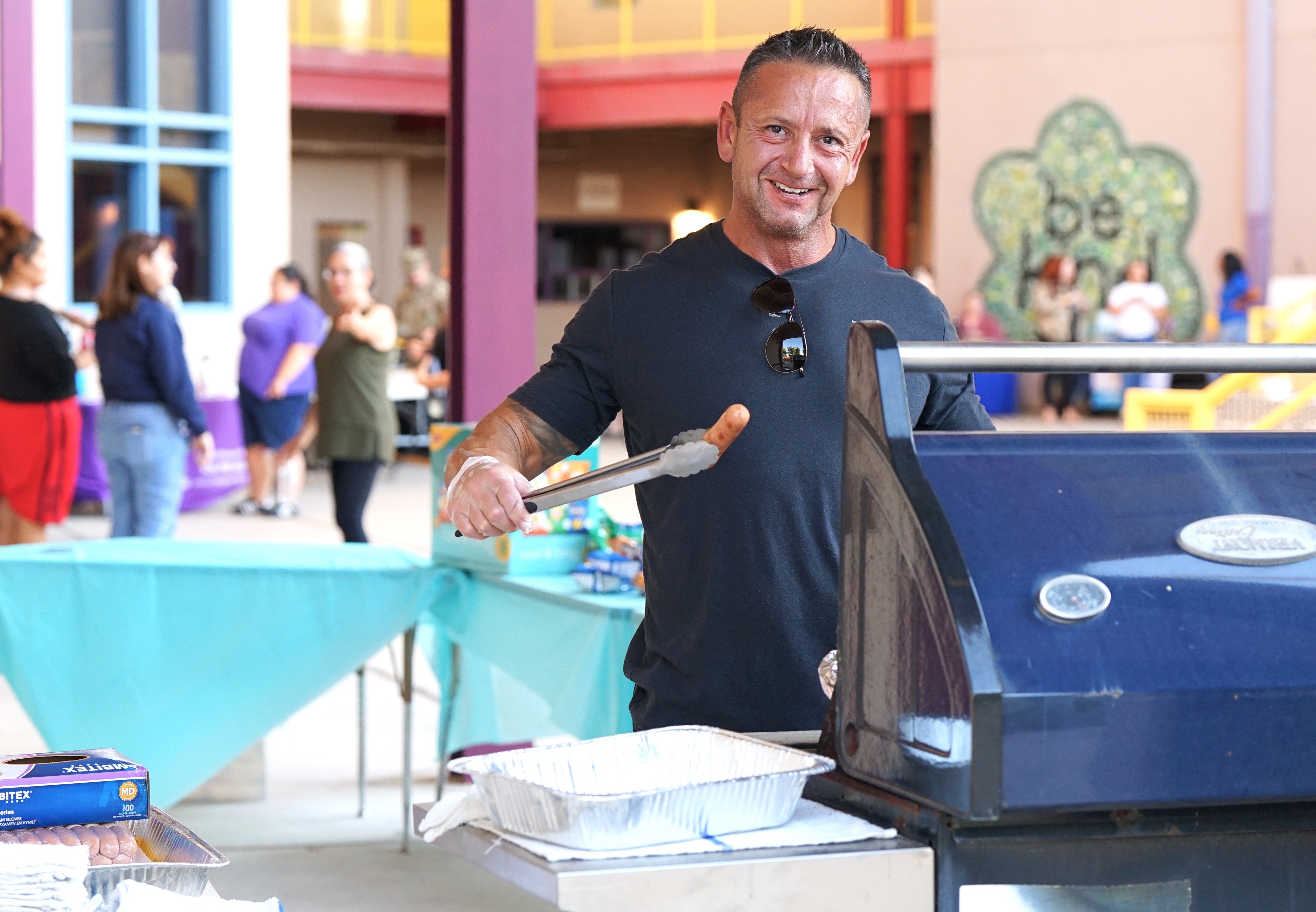 A man smiles as he cooks hot dogs on the grill