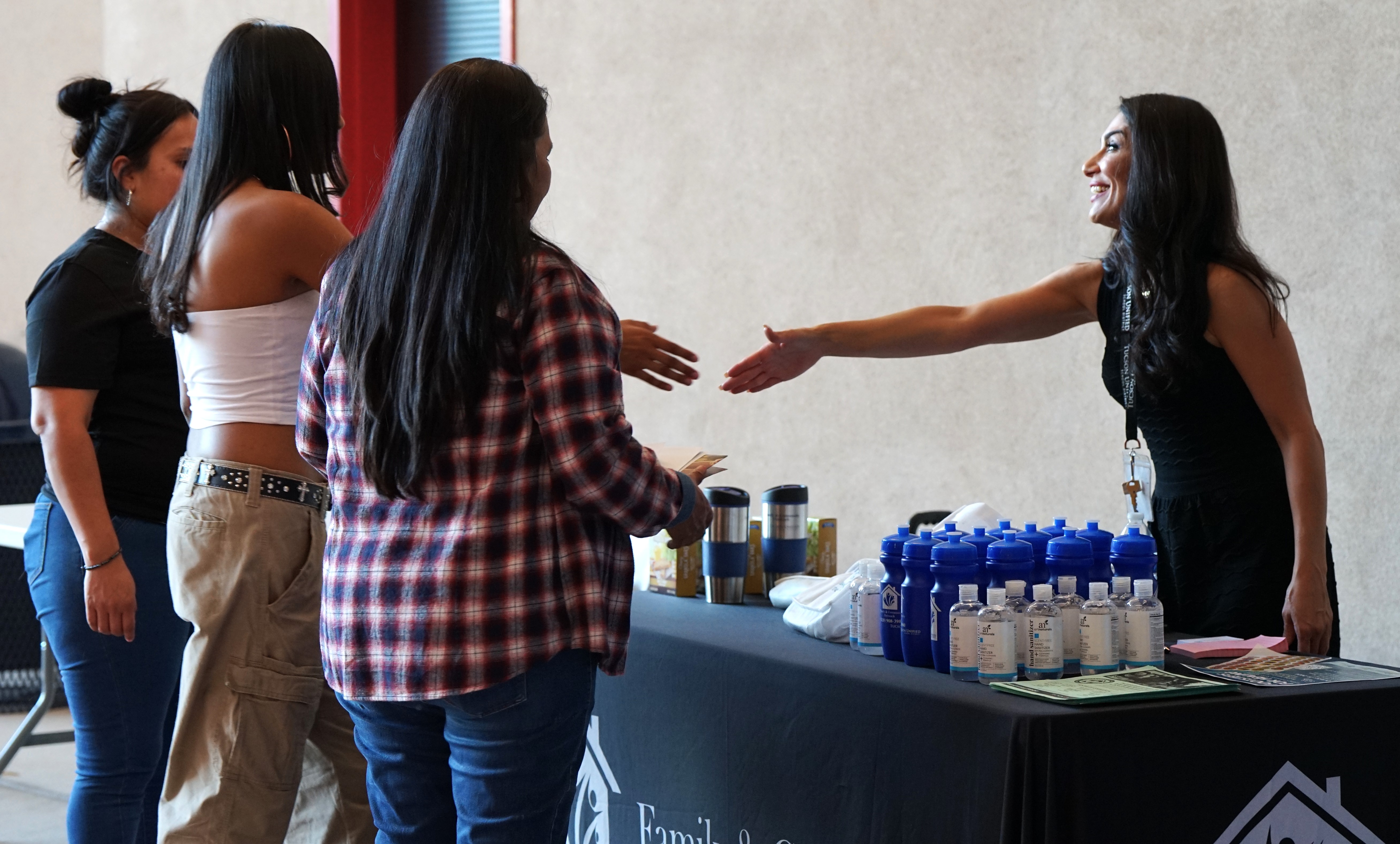 A woman shakes hands with students from behind her table at the fair