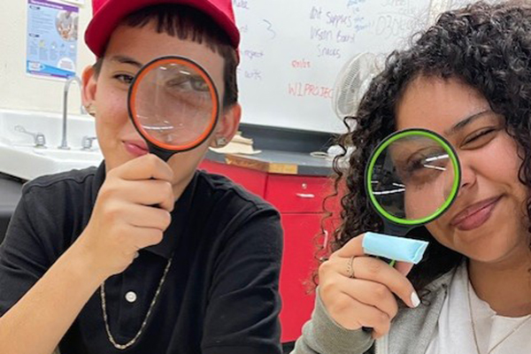 Two students hold magnifying glasses to their eyes