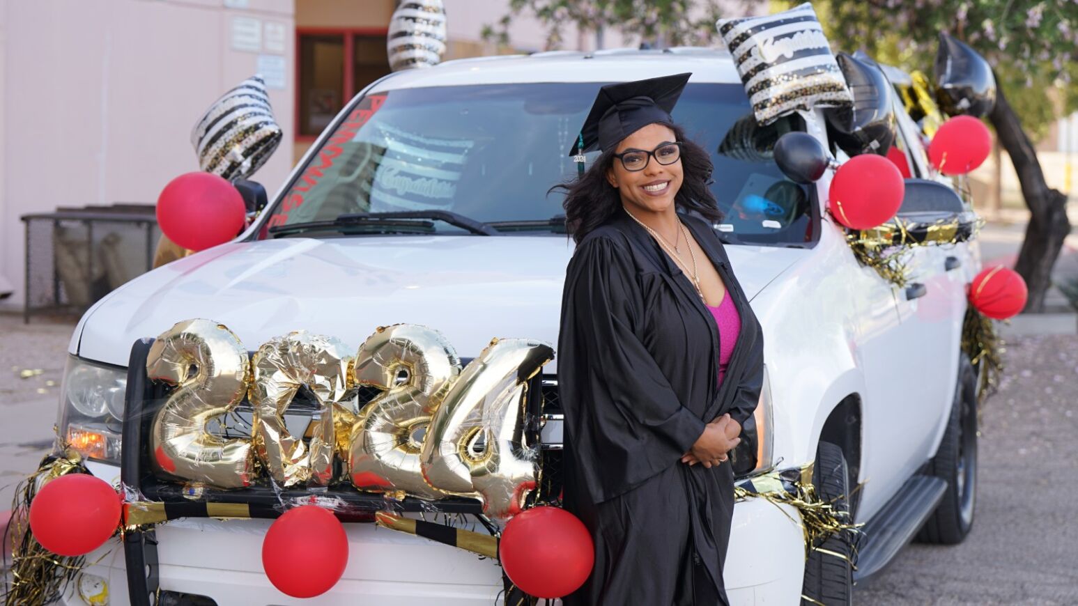 A Project MORE grad smiles in front of a white SUV decked out in graduation balloons